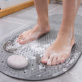 Person using a gray bath mat with holes to scrub feet in a bathtub filled with water and soap suds.