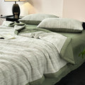 Close-up of soft green cotton gauze quilt and pillowcases on dark wood bed