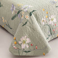 Close-up of green floral cotton quilt showing texture, stitching, and floral print