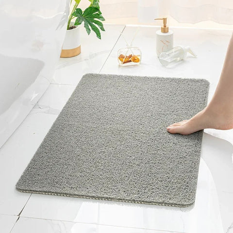 Gray bath mat on a bathroom floor with a foot stepping onto it