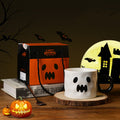 Halloween-themed mug with ghost design, pumpkin, and gift box on a wooden surface.