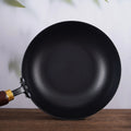 Top view of hammer pattern iron wok pan with wooden handle on wooden surface