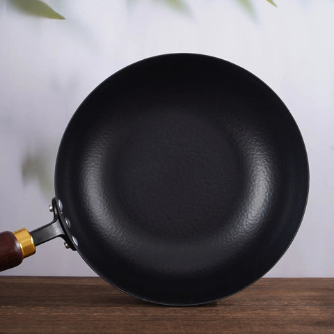 Top view of hammer pattern iron wok pan with wooden handle on wooden surface