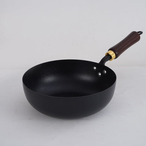 Hammer pattern iron wok pan with wooden handle on white surface