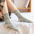 Model wearing pastel green embroidered floral socks with vintage Japanese-inspired design, sitting on a white bed.