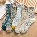A collection of four socks with various floral designs, placed on a wooden surface with a textured background.