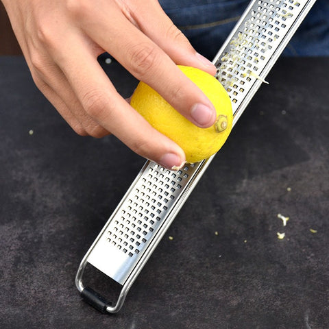 Hand grating lemon zest with a wooden handle stainless steel grater over dark surface