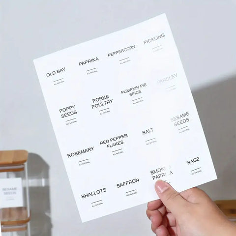 Close-up of a hand holding a minimalist black and white spice label sticker sheet.

