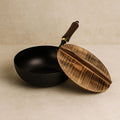Handmade iron wok pan with wooden lid resting on white surface