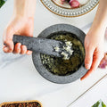 Hands crushing herbs with vintage marble mortar and pestle on white kitchen surface