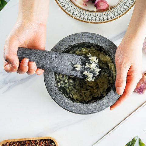 Hands crushing herbs with vintage marble mortar and pestle on white kitchen surface