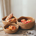 Three handwoven rattan fruit baskets with bread and apples on wooden table