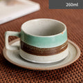 Ceramic cup with a brown stripe on a saucer, placed on a textured surface.
