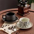 Two ceramic cups with saucers on a table with coffee beans and a wooden grinder.