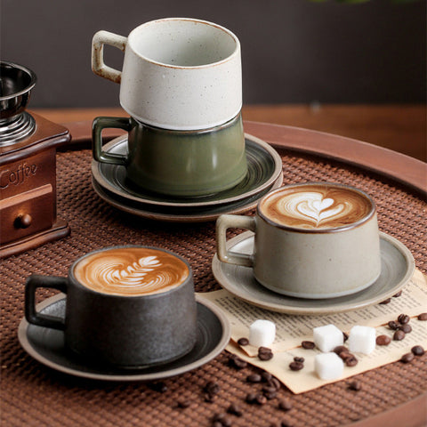 Three ceramic coffee cups with latte art on a wooden table with coffee beans and a grinder.