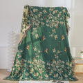 Green floral-patterned blanket draped over a surface with a white curtain in the background.
