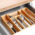 Wooden cutlery organizer with silverware inside a kitchen drawer.