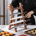 Set of knives on a wooden stand with a person in a black apron in the background.
