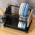 Black dish rack with plates, glasses, and utensils on a wooden countertop.