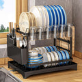 Black dish drying rack with plates, glasses, and cutlery on a wooden surface.