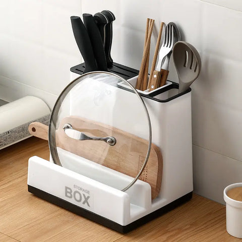 White kitchen utensil storage box with cutting board, lid, and utensils on a wooden countertop.