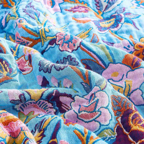 Close-up of Lavender Meadow Cotton Blanket fabric showing detailed floral embroidery in pastel colors with birds on light blue background