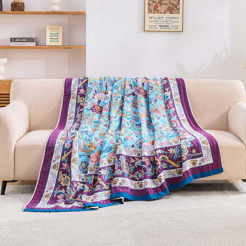 Lavender Meadow Cotton Blanket draped over beige sofa in cozy living room with natural light, showcasing vibrant floral and bird patterns in blue, purple, and pink tones
