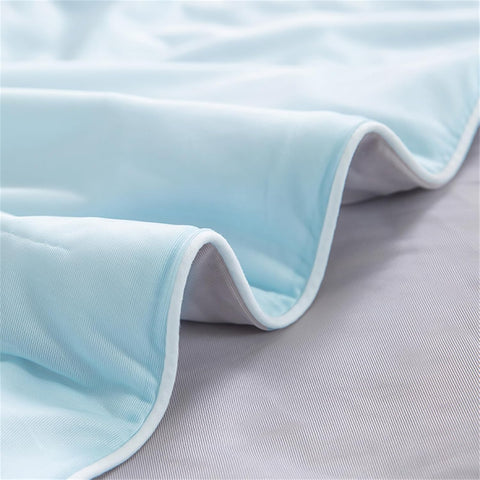 Detailed close-up of light blue ice silk quilt fabric edge, highlighting fine stitching and silky finish.