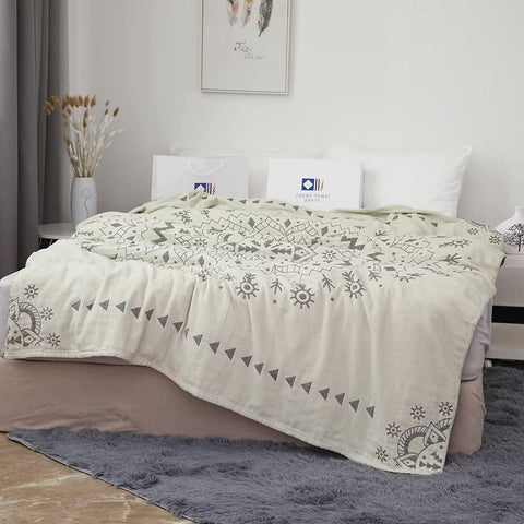Cozy beige cotton boho throw blanket with intricate gray patterns draped over a bed in a bright, minimalist bedroom setting.