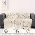  Beige cotton boho throw blanket with gray tribal patterns draped over a gray sofa, showing care icons for machine wash, gentle cycle, and no bleach.