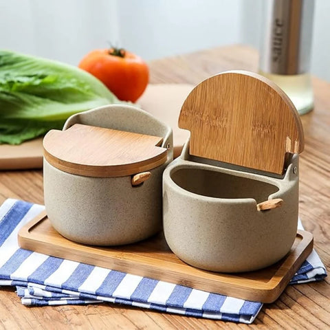Two ceramic containers with wooden lids on a wooden tray with a striped cloth underneath.