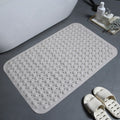 Khaki textured bath mat on a bathroom floor with a bathtub and slippers in the background.