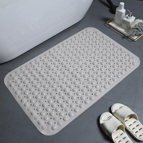 Khaki textured bath mat on a bathroom floor with a bathtub and slippers in the background.
