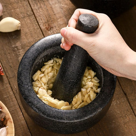 Hands crushing garlic cloves in a granite mortar and pestle on wooden surface