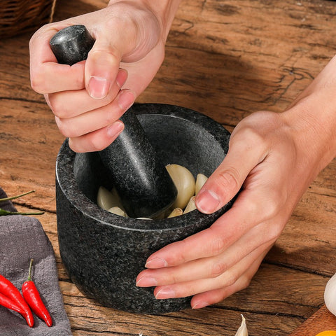 Hands crushing garlic cloves in a natural granite mortar with pestle on wooden surface