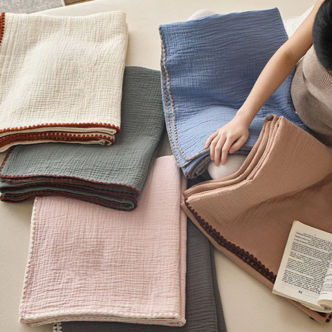 Assorted muslin cotton blankets in neutral and pastel colors on beige sofa