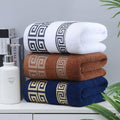 Stack of three folded towels with geometric patterns on a surface with books and a bottle.