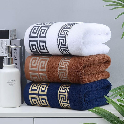 Stack of three folded towels with geometric patterns on a surface with books and a bottle.