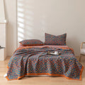Bed with patterned blue and orange bedding in a room with wooden floor and white walls.