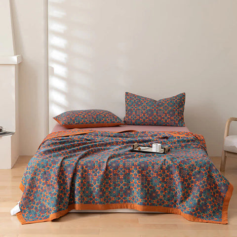 Bed with patterned blue and orange bedding in a room with wooden floor and white walls.
