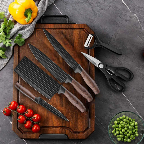 Set of knives on a wooden cutting board with vegetables and kitchen tools on a gray surface