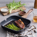 Black cast iron skillet with steak and asparagus on a gray surface with greens and a glass of beer.