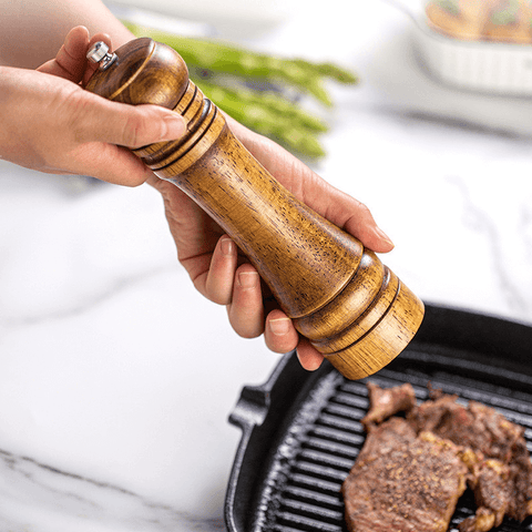 Hand using oakwood pepper grinder over grilled food