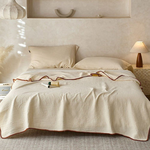 Off-white cotton muslin blanket on neatly styled bed with neutral decor