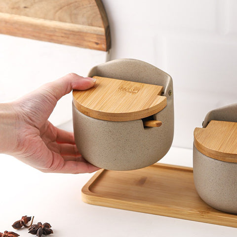 Hand holding a beige ceramic container with a wooden lid on a white background