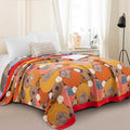 Persimmon Bloom cotton blanket with vibrant floral pattern spread over queen bed in cozy bedroom setting