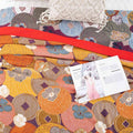 Persimmon Bloom cotton blanket folded on bed with macrame pillow and open magazine