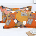 Pair of Persimmon Bloom cotton pillowcases with vibrant floral and persimmon pattern in orange, pink, and gray on a dark background, displayed on a white bed next to a wooden tray with a white cup.