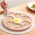 Hand holding pink Animals Waffle and Pancake Pan with cooked egg in center on wooden table