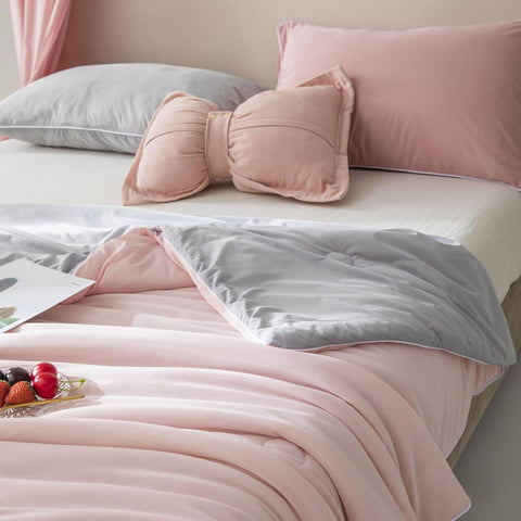 Cozy bedroom scene with light pink and gray ice silk quilt draped over bed, featuring matching pillows and soft natural light.
